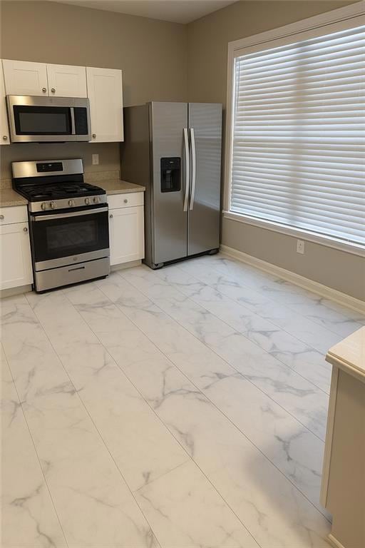Kitchen with appliances with stainless steel finishes, light marble finish flooring, and white cabinets