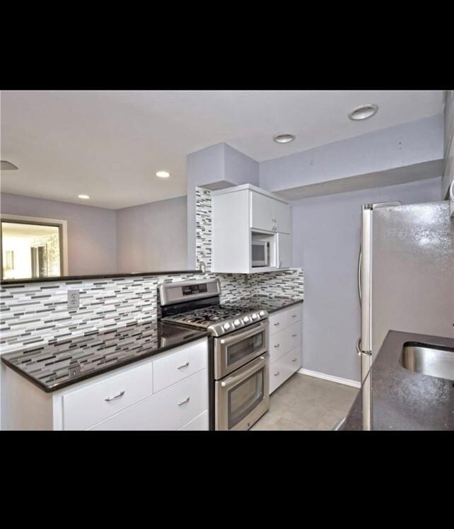 Kitchen featuring stainless steel appliances, white cabinets, decorative backsplash, dark stone countertops, and recessed lighting