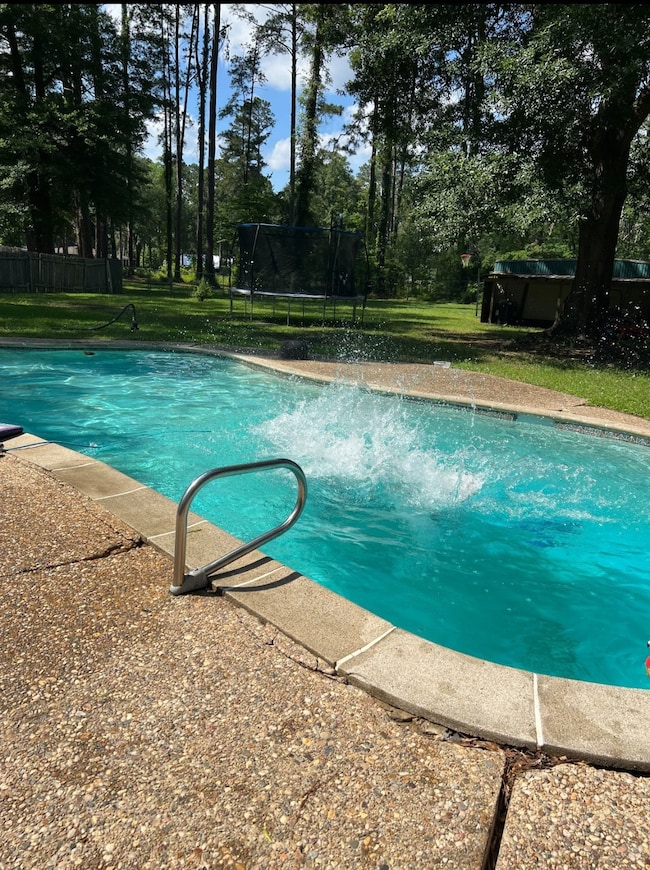 View of swimming pool with a trampoline, a yard, and view of wooded area