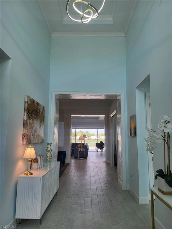 Corridor featuring wood finished floors, a towering ceiling, ornamental molding, a chandelier, and a tray ceiling