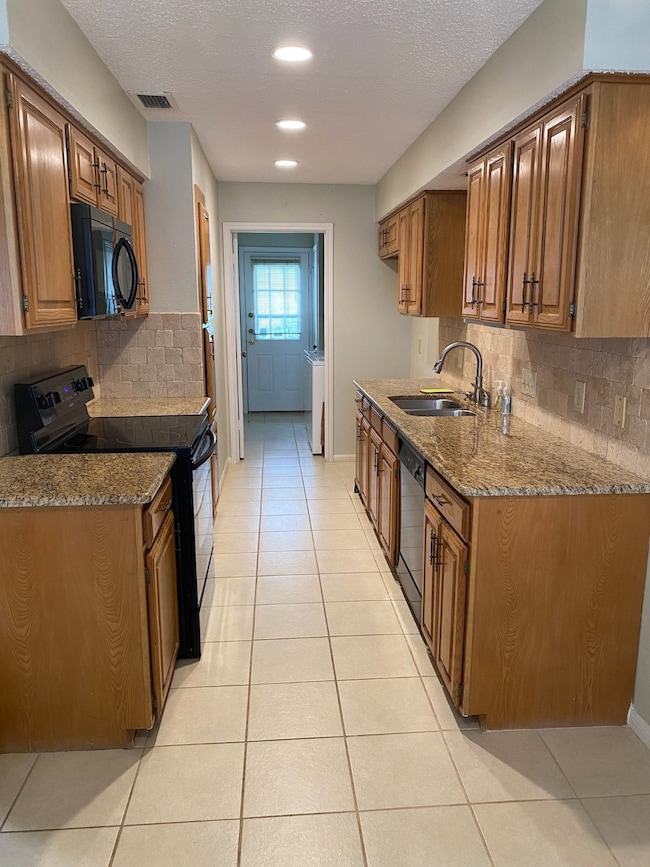 Kitchen with backsplash, black appliances, brown cabinets, light stone counters, and a textured ceiling