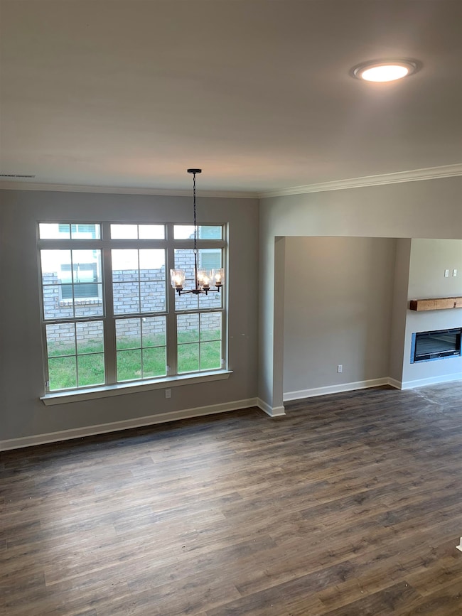 Unfurnished dining area featuring ornamental molding, a chandelier, dark wood-style flooring, and a fireplace