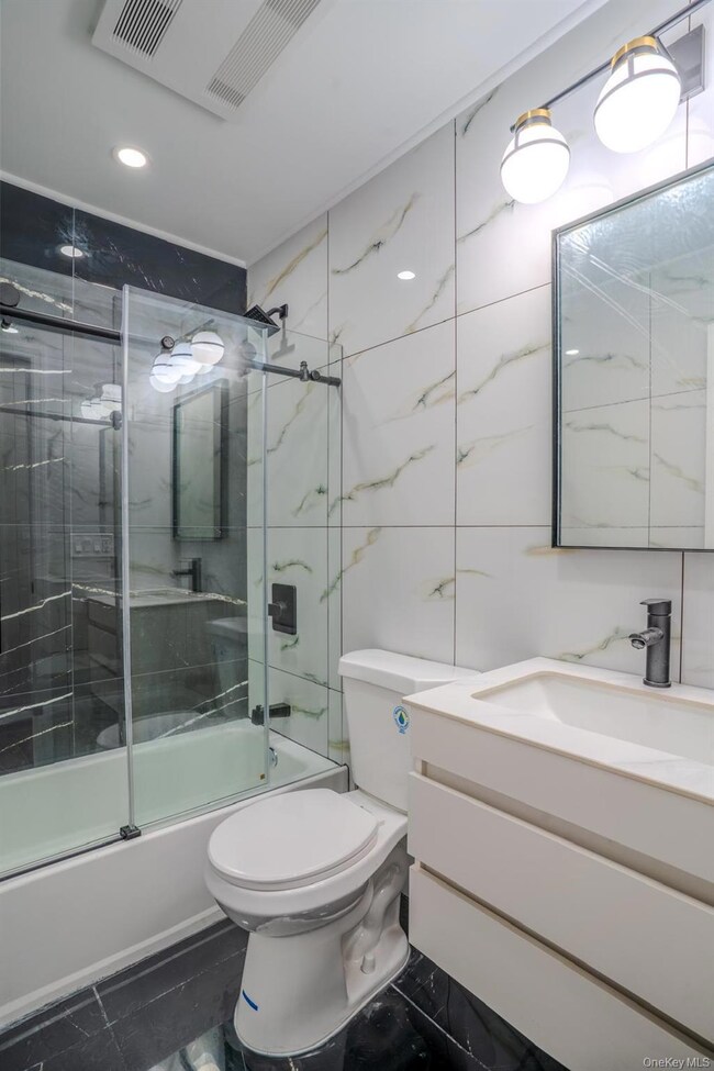 Bathroom with vanity, bath / shower combo with glass door, tile walls, and recessed lighting