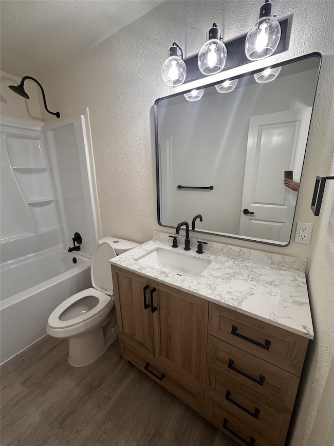 Bathroom with a textured wall, vanity, shower / bathtub combination, dark wood finished floors, and a textured ceiling