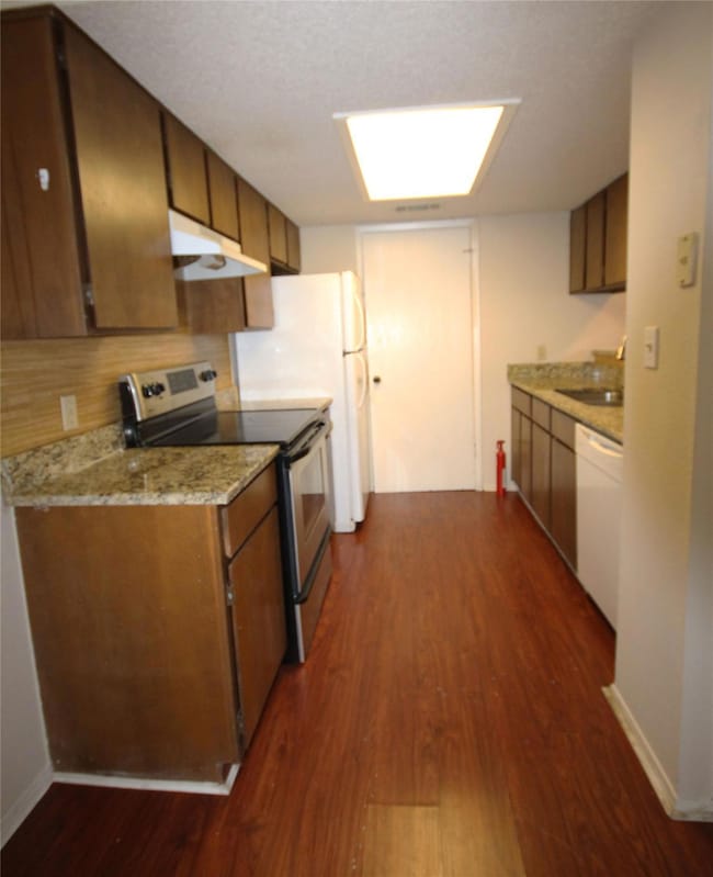 Kitchen with stainless steel electric stove, dark wood-style flooring, under cabinet range hood, light stone counters, and white dishwasher
