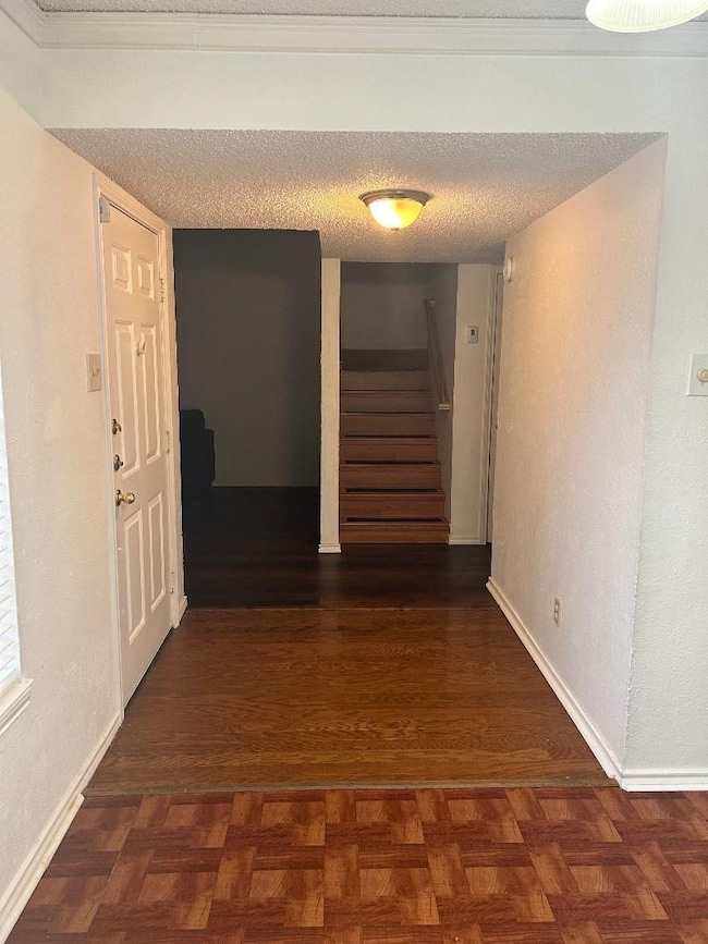 Hallway with stairway, a textured wall, a textured ceiling, and parquet floors