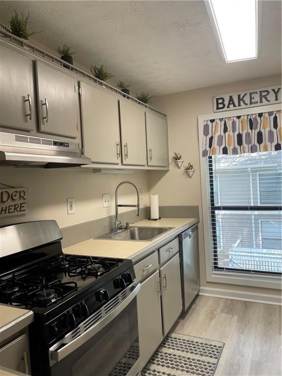 Kitchen featuring stove, range hood, light wood-style floors, light countertops, and dishwasher