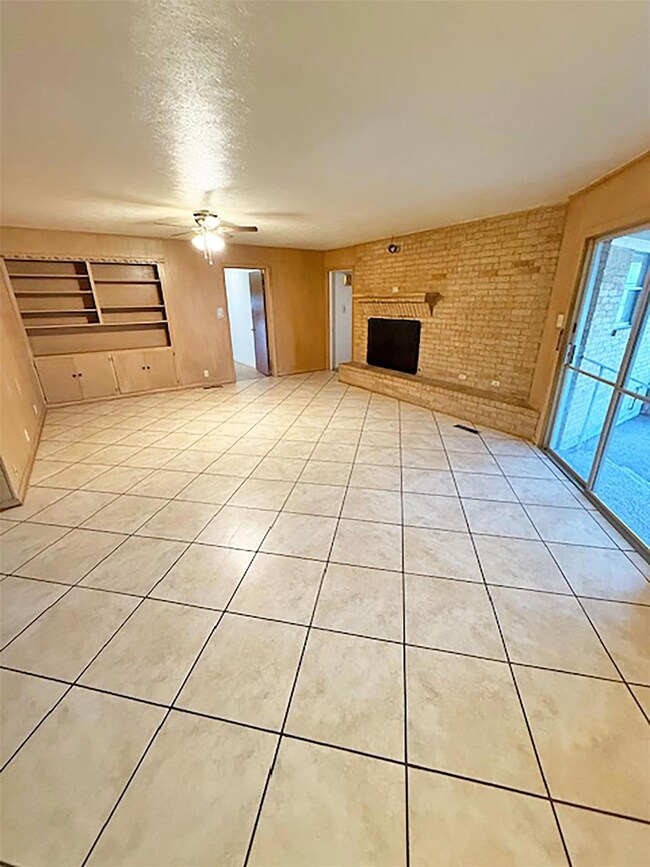 Unfurnished living room with light tile patterned floors, ceiling fan, a textured ceiling, brick wall, and a brick fireplace