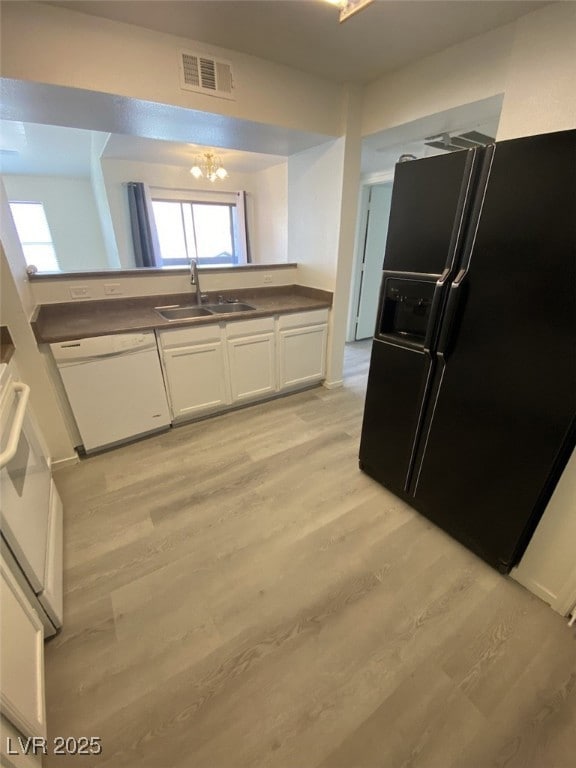Kitchen with white appliances, white cabinetry, light wood-style flooring, dark countertops, and a chandelier