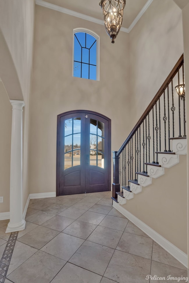 Tiled entrance foyer with crown molding, healthy amount of natural light, arched walkways, stairway, and ornate columns