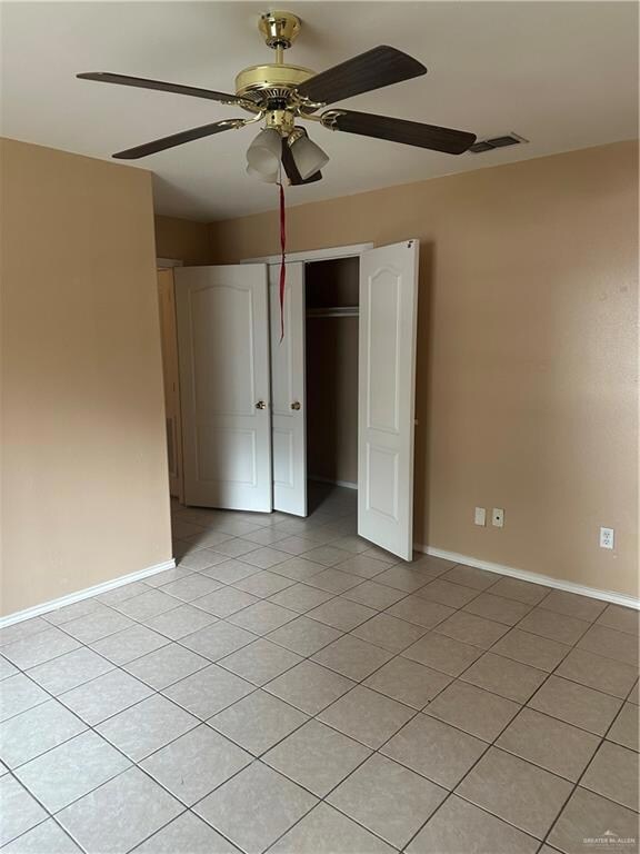 Unfurnished bedroom featuring light tile patterned floors, a closet, visible vents, ceiling fan, and baseboards