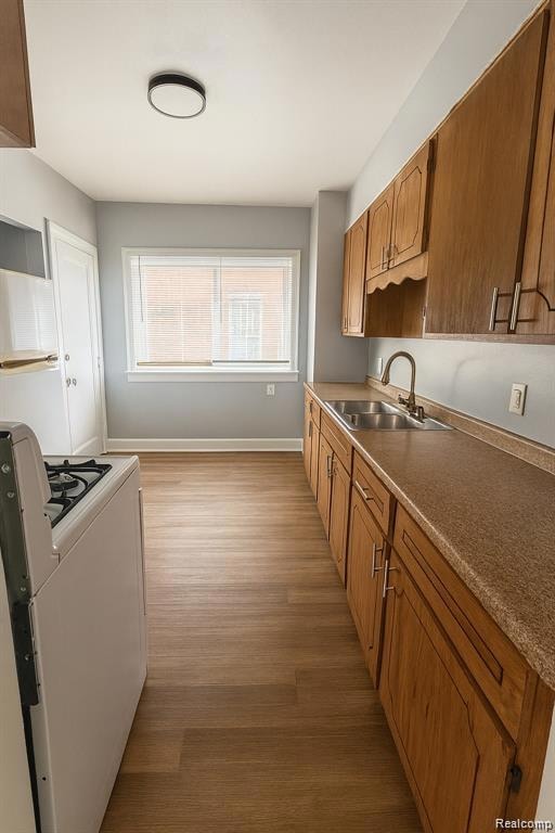 Kitchen with white range with gas stovetop, light wood-style flooring, brown cabinets, and light countertops