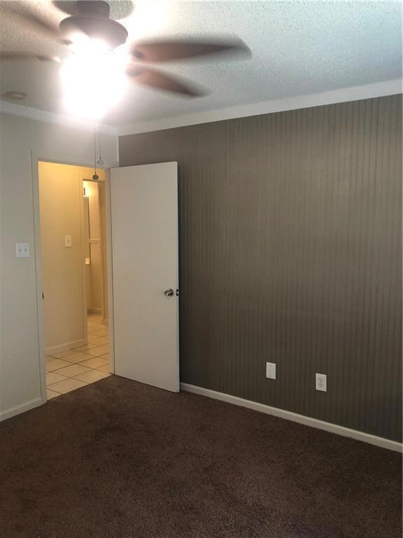 Unfurnished room featuring light carpet, a textured ceiling, wooden walls, crown molding, and ceiling fan