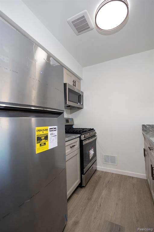 Kitchen featuring appliances with stainless steel finishes, light wood finished floors, white cabinets, and light stone counters