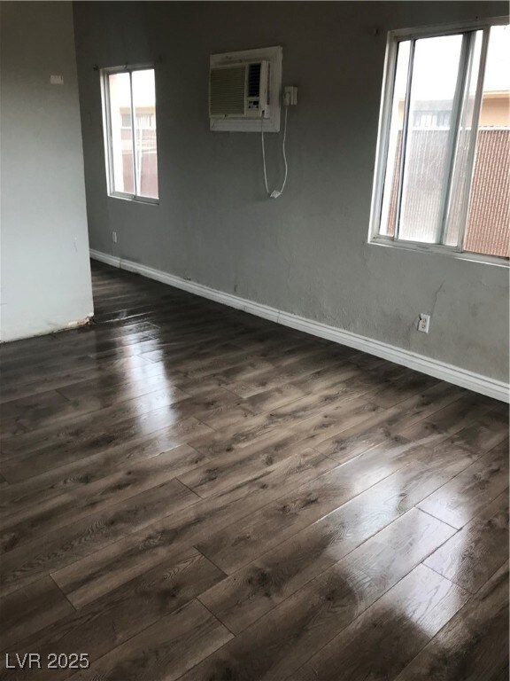 Spare room featuring baseboards, a wall unit AC, and dark wood-style flooring