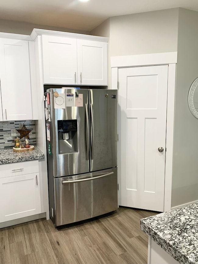 Kitchen with stainless steel fridge with ice dispenser, white cabinetry, light wood finished floors, and light stone counters