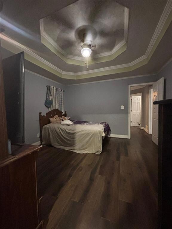 Bedroom with a raised ceiling, crown molding, dark wood-style flooring, and ceiling fan