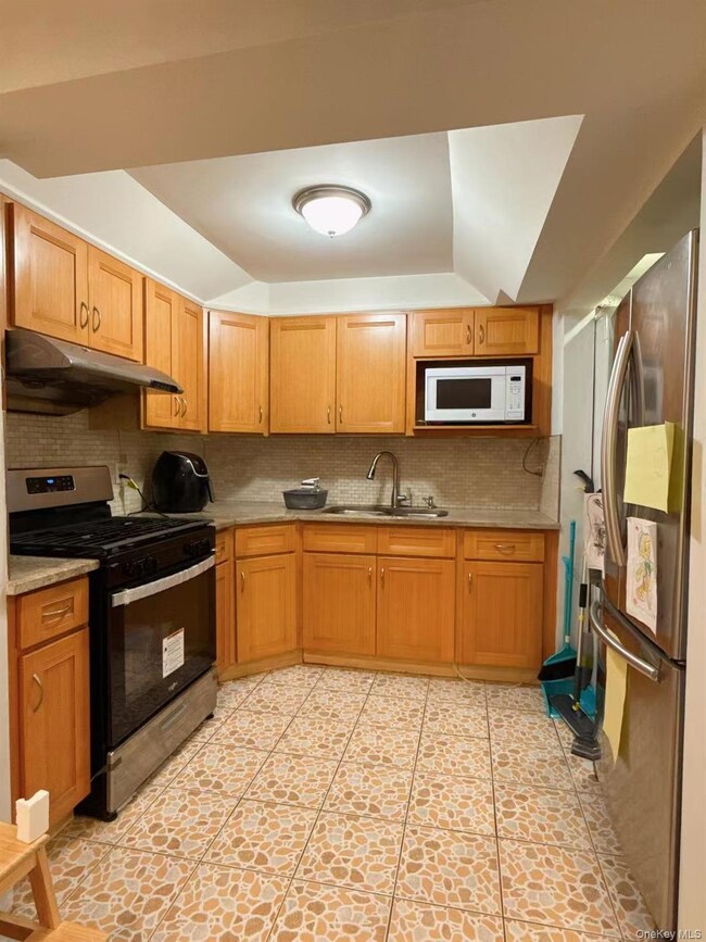 Kitchen with decorative backsplash, stainless steel appliances, under cabinet range hood, and brown cabinets