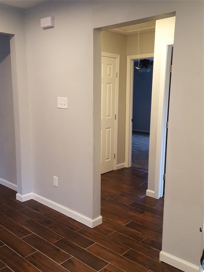 Hallway to Spacious Guest Bath,  Bedroom 2, and Bedroom 3 - Total Renovation  See neutral color Carpet and wallpaint.  Bright white baseboard and hardwood tile flooring throughout the home.