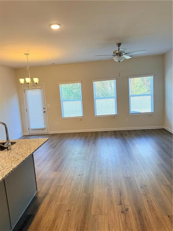 Unfurnished living room featuring healthy amount of natural light, dark wood-style floors, a ceiling fan, recessed lighting, and a chandelier