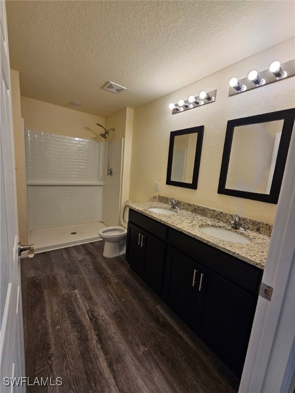 Bathroom featuring wood finished floors, double vanity, tiled shower, and a textured ceiling