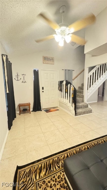 Tiled entryway featuring a textured ceiling, a ceiling fan, stairway, lofted ceiling, and baseboards