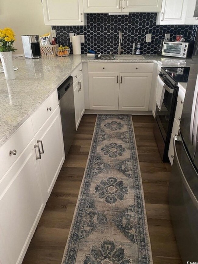 Kitchen with dark wood finished floors, white cabinetry, stainless steel appliances, and a sink
