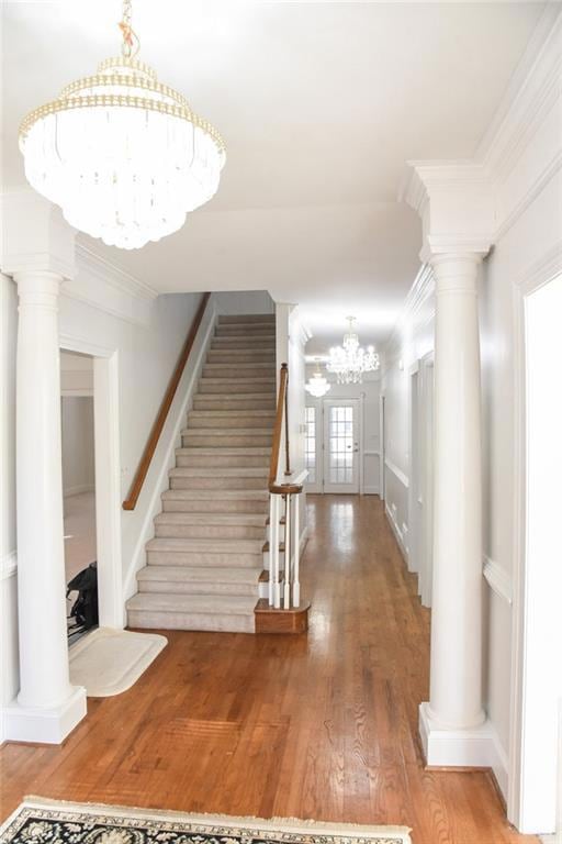 Stairs with a chandelier, ornate columns, ornamental molding, and wood finished floors