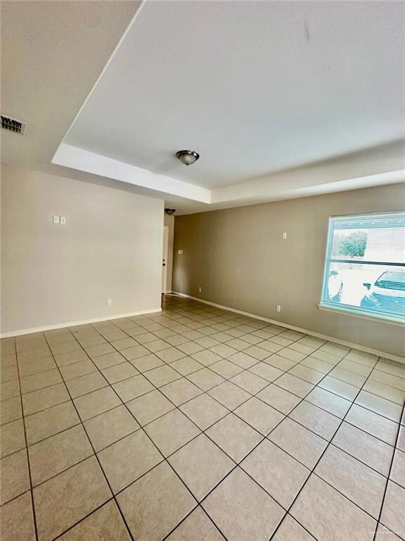 Empty room with light tile patterned flooring and a tray ceiling