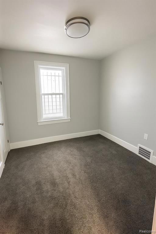 Empty room featuring dark carpet and baseboards