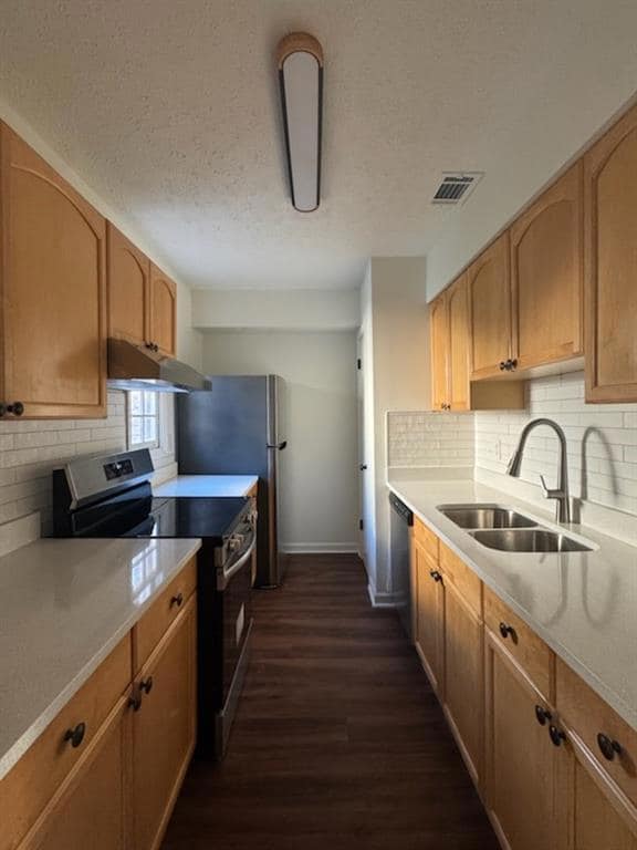 Kitchen featuring stainless steel appliances, dark wood-type flooring, a textured ceiling, light countertops, and backsplash
