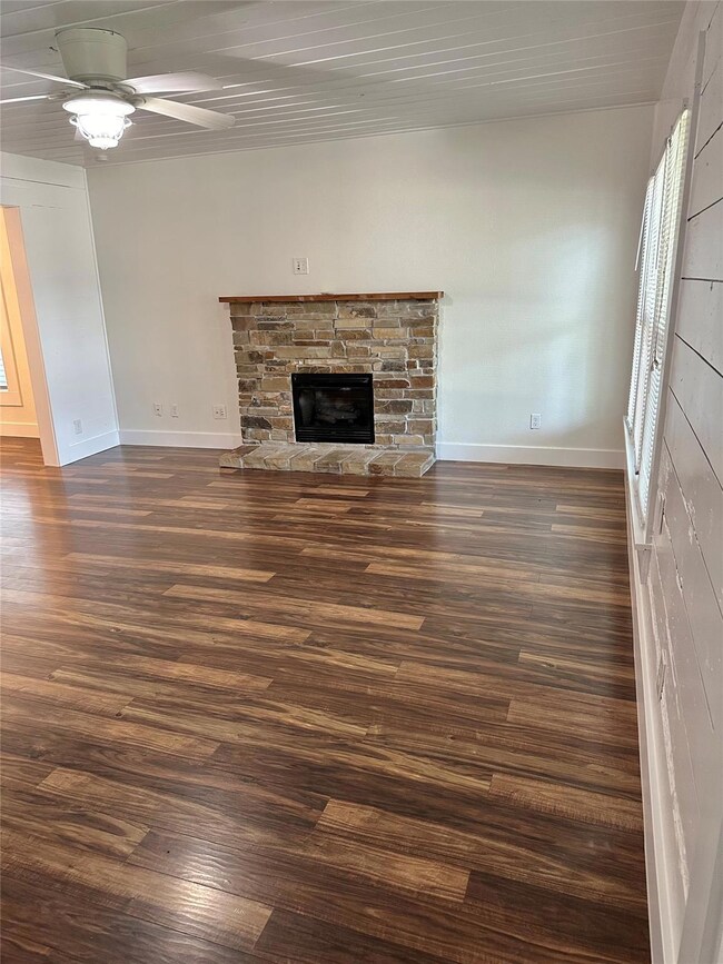 Unfurnished living room with dark wood-type flooring, ceiling fan, and a fireplace