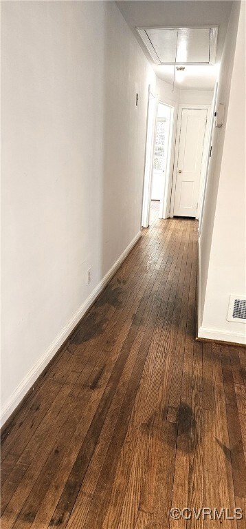 Hallway with attic access, baseboards, and dark wo