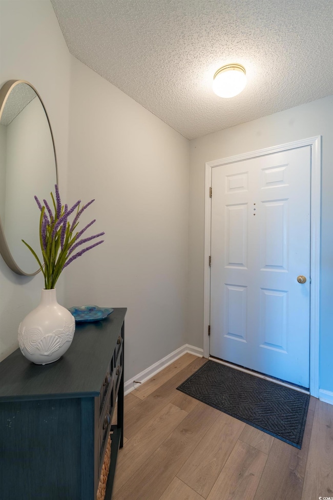 Foyer with baseboards, a textured ceiling, and woo
