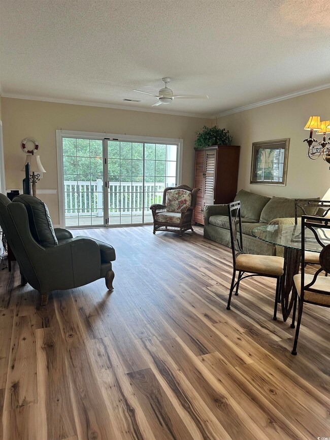 Living room featuring ornamental molding, a textured ceiling, wood finished floors, and a ceiling fan