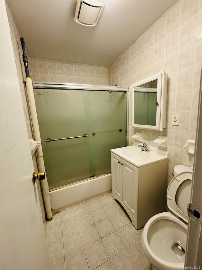 Bathroom with combined bath / shower with glass door, tile walls, light tile patterned floors, and vanity