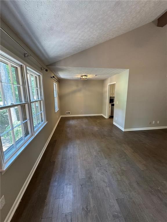 Empty room with vaulted ceiling, a textured ceiling, and dark wood-style flooring