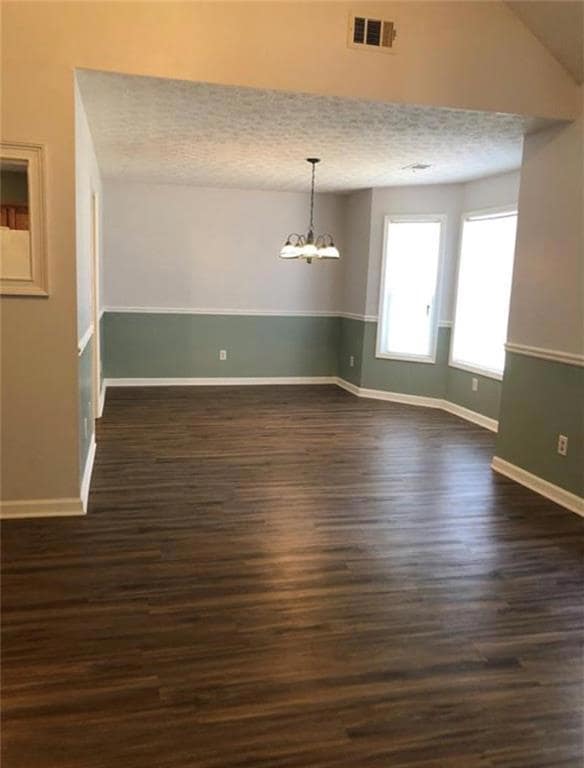 Spare room featuring a chandelier, dark wood-type flooring, a textured ceiling, and lofted ceiling