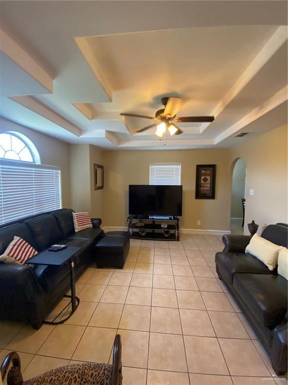 Living area featuring a tray ceiling, arched walkways, ceiling fan, and light tile patterned floors