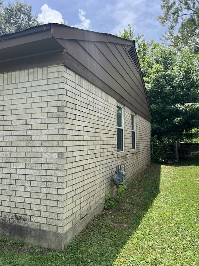 View of side of property featuring a lawn and brick siding