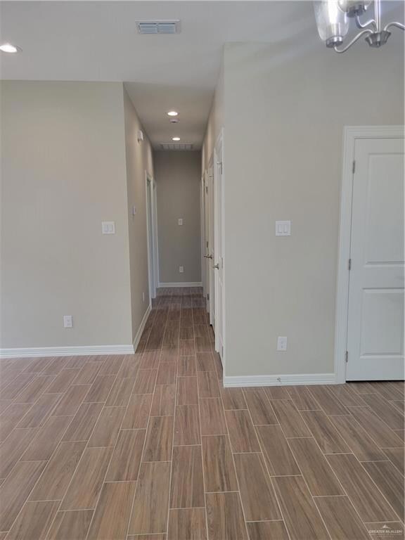 Empty room featuring light wood-type flooring and an inviting chandelier