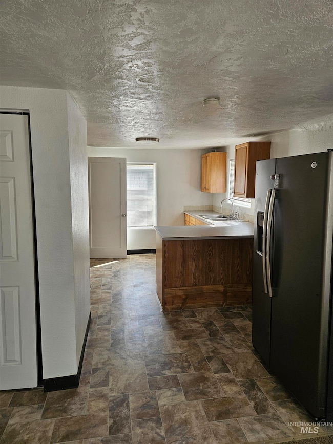 Kitchen with stainless steel fridge with ice dispenser, light countertops, brown cabinetry, a peninsula, and a textured ceiling