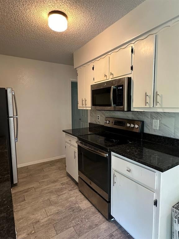 Kitchen featuring appliances with stainless steel finishes, backsplash, a textured ceiling, light wood-style flooring, and dark stone counters