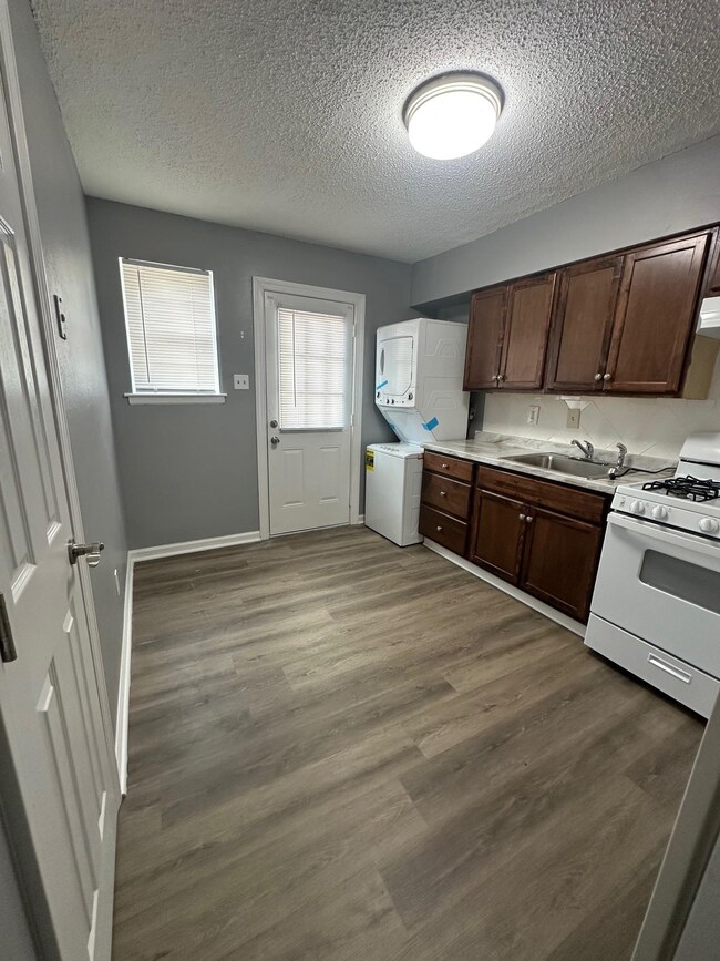 Kitchen featuring white gas range oven, a textured ceiling, stacked washer / drying machine, light countertops, and dark brown cabinetry