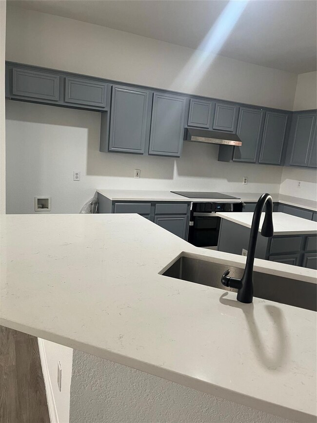 Kitchen featuring gray cabinets, ventilation hood, wall oven, cooktop, and dark wood-type flooring