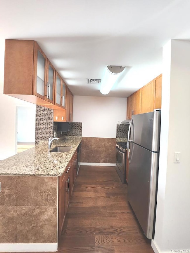 Kitchen featuring dark wood-type flooring, glass insert cabinets, decorative backsplash, stainless steel appliances, and light stone counters