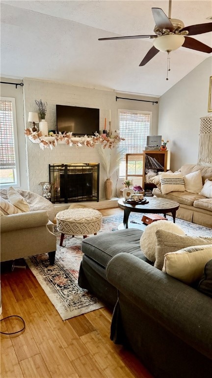 Living room with wood finished floors, ceiling fan, a large fireplace, lofted ceiling, and a textured ceiling