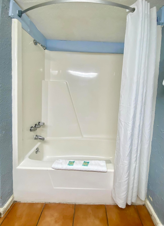 Full bath featuring a textured wall, shower / bath combo with shower curtain, and tile patterned floors