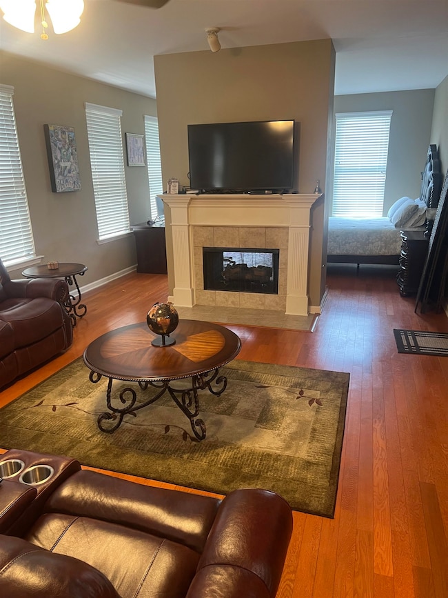 Living area featuring dark wood finished floors, a tiled fireplace, ceiling fan, and baseboards