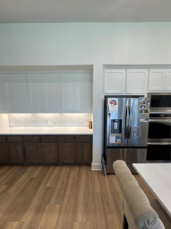 Kitchen featuring fridge, white cabinetry, dark brown cabinets, dark wood finished floors, and double wall oven
